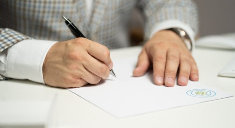 Mann im Anzug unterschreibt mit Kugelschreiber ein Dokument.
